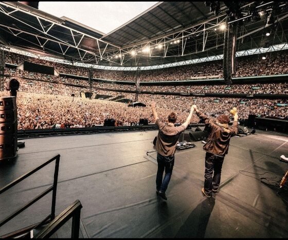 Oasis lança Aquiesce ao vivo em Wembley na coletânea HELP(2) da War Child; gravação sai em single 7” avulso, CD e streaming nesta sexta-feira.